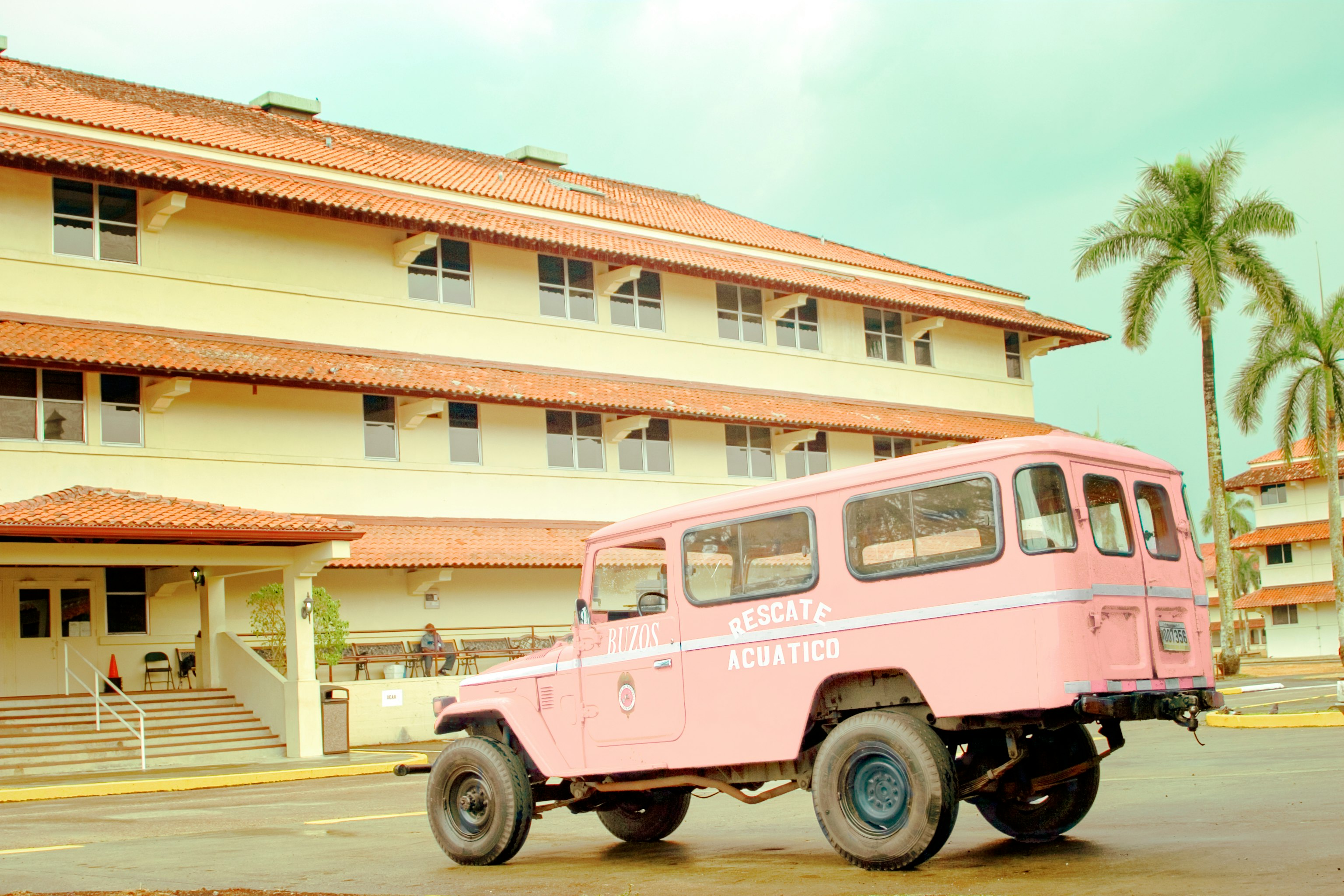 pink and white vintage car parked in front of white and brown concrete building during daytime